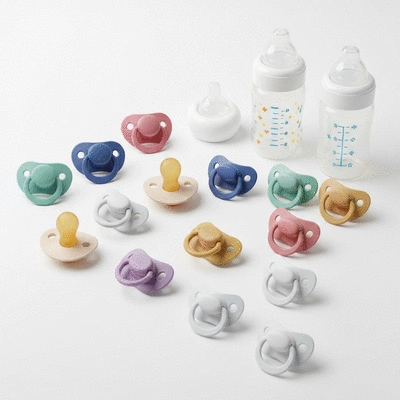 Zbliżenie na różne rodzaje smoczków i butelek antykolkowych ułożonych na białym tle